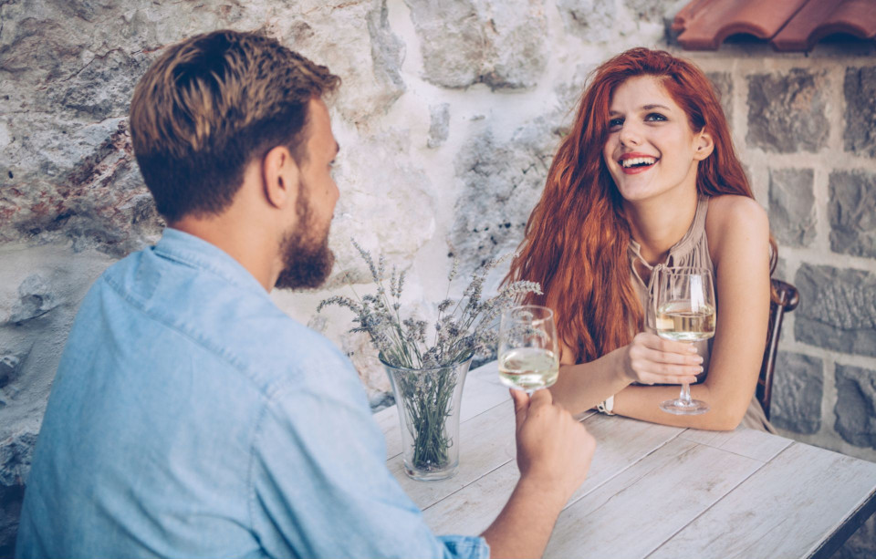 man and woman sitting across from each other drinking wine and smiling